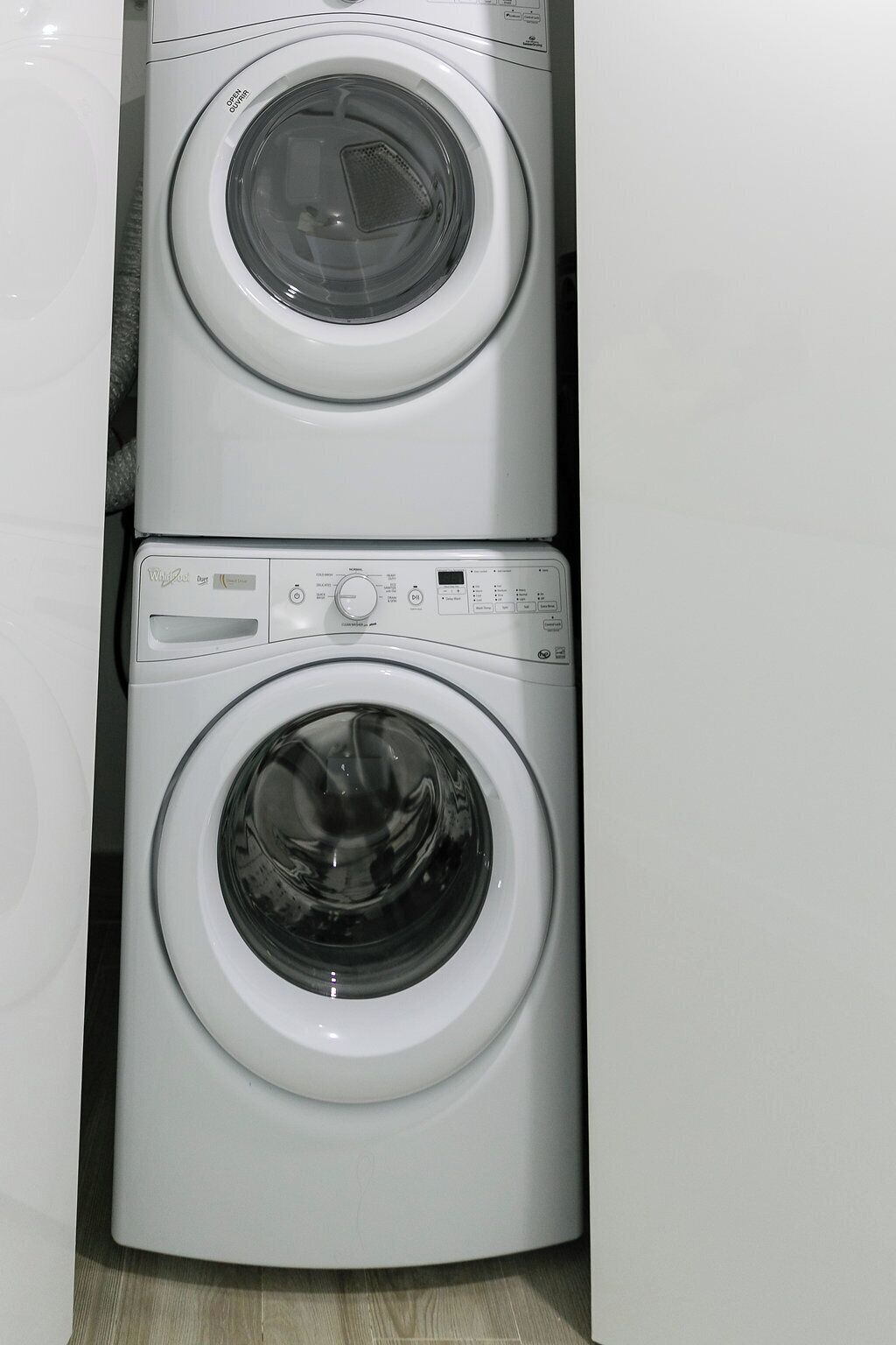 Un appareil combiné lave-linge et sèche-linge, de type « empilable », doté de panneaux de commande et d’une porte transparente.