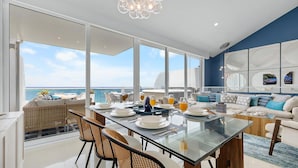 A modern dining area with a glass table, wicker chairs, and a view of the ocean.