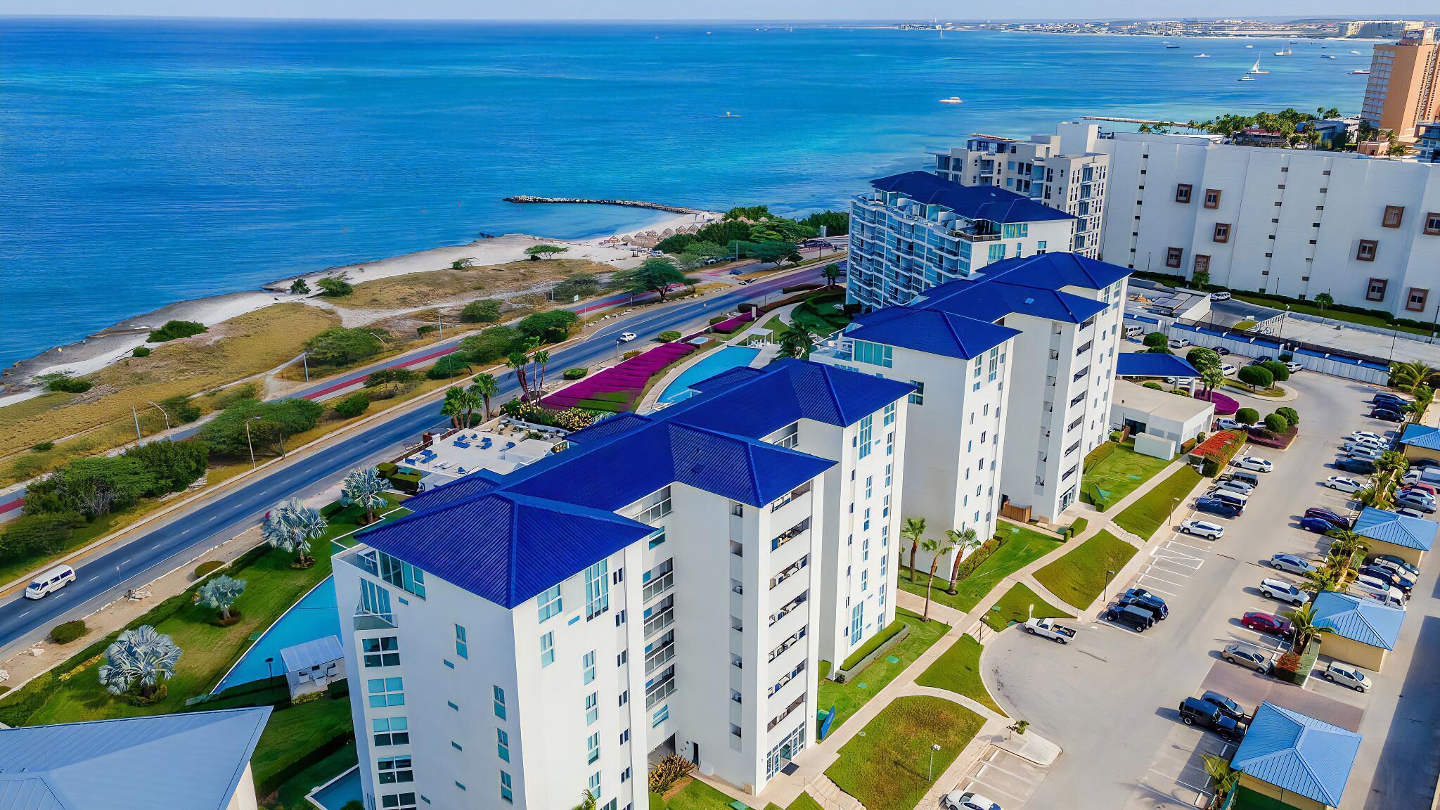 A high-rise hotel with multiple floors, a parking area, and a view of the ocean.