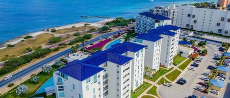 A high-rise hotel with multiple floors, a parking area, and a view of the ocean.