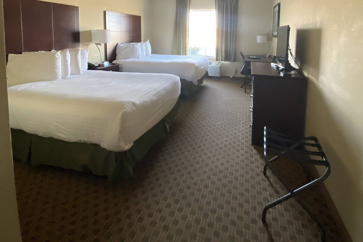 Een hotelkamer met twee bedden, een bureau, een stoel, een televisie en een raam met gordijnen.