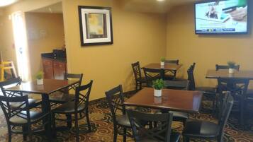 A restaurant with multiple tables and chairs, a framed picture on the wall, and a television displaying an advertisement.
