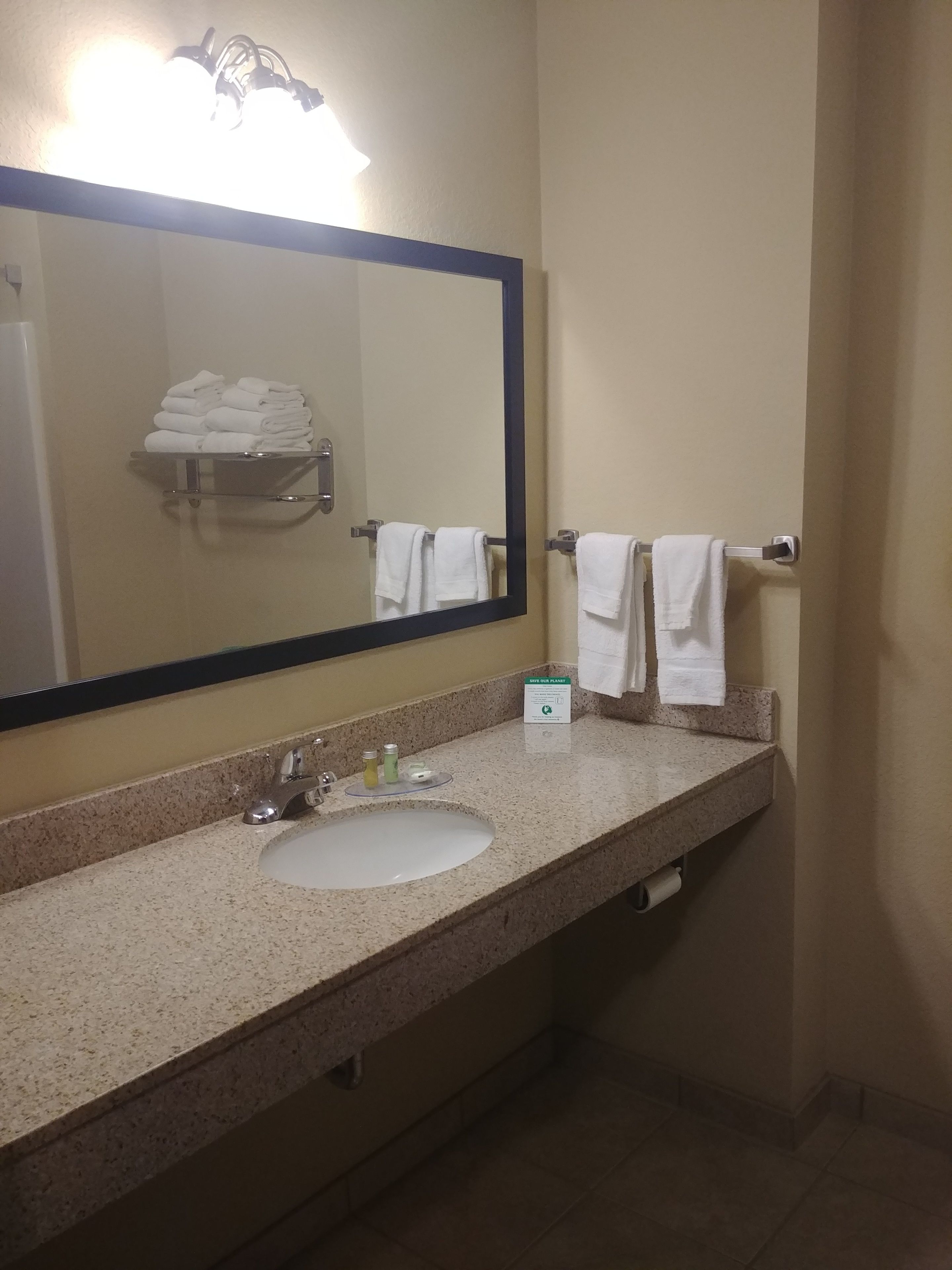 A bathroom with a sink, mirror, towel rack, and a 'SAVE OUR PLANET' sign.
