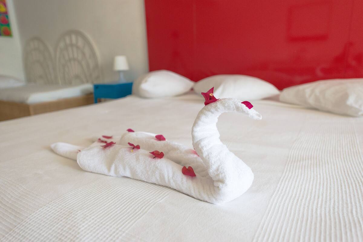 A neatly made swan-shaped bedspread with rose petals on a hotel bed.