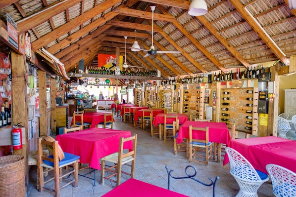 Un restaurant avec des tables et des chaises en bois, des nappes rouges et une variété de bouteilles exposées sur des étagères.