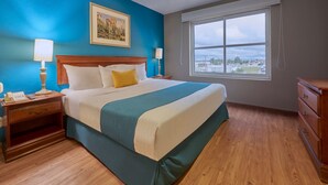 A hotel room with a large bed, wooden nightstands, a dresser, a window with a city view, and a painting on the wall. - Hotel Sierra by HP Hotels (San Luis Potosi)