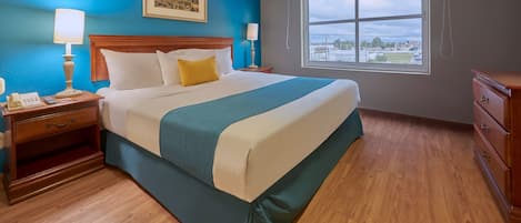 Habitación de hotel con una cama grande, mesitas de noche de madera, un aparador, una ventana con vista a la ciudad y un cuadro en la pared.