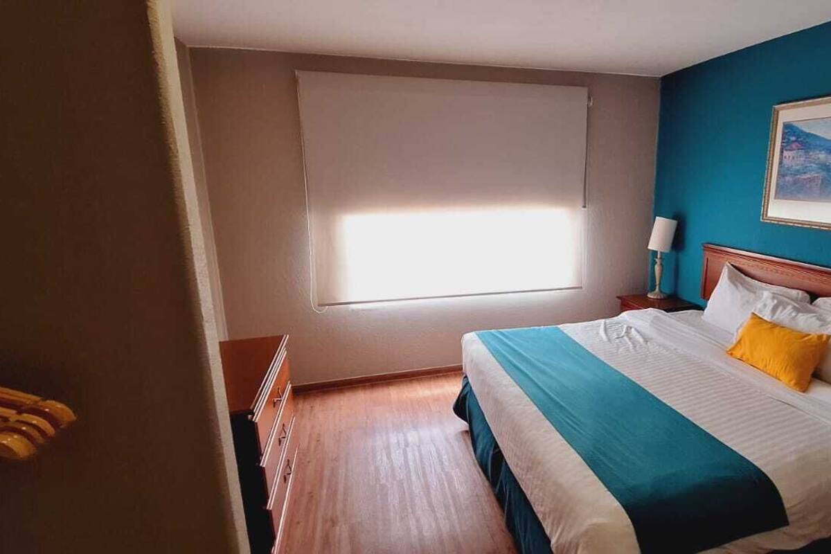 Una habitación de hotel con una cama, ventana, un cuadro en la pared y suelo de madera.