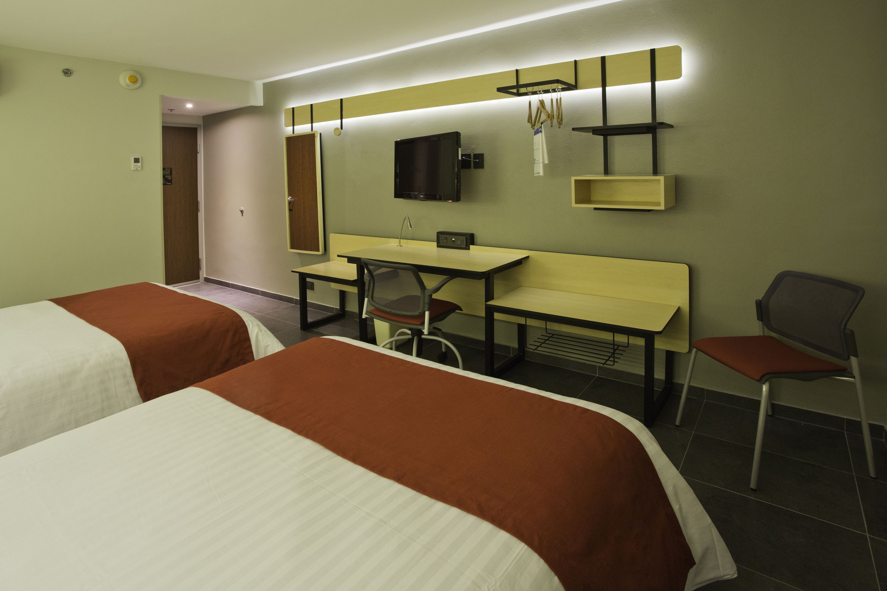 Habitación de hotel con dos camas, un escritorio, una silla, un televisor y un espejo.