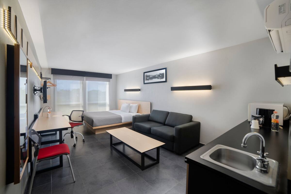 Een moderne hotelkamer met een bed, een slaapbank, een eettafel en een keukenhoek met een spoelbak.