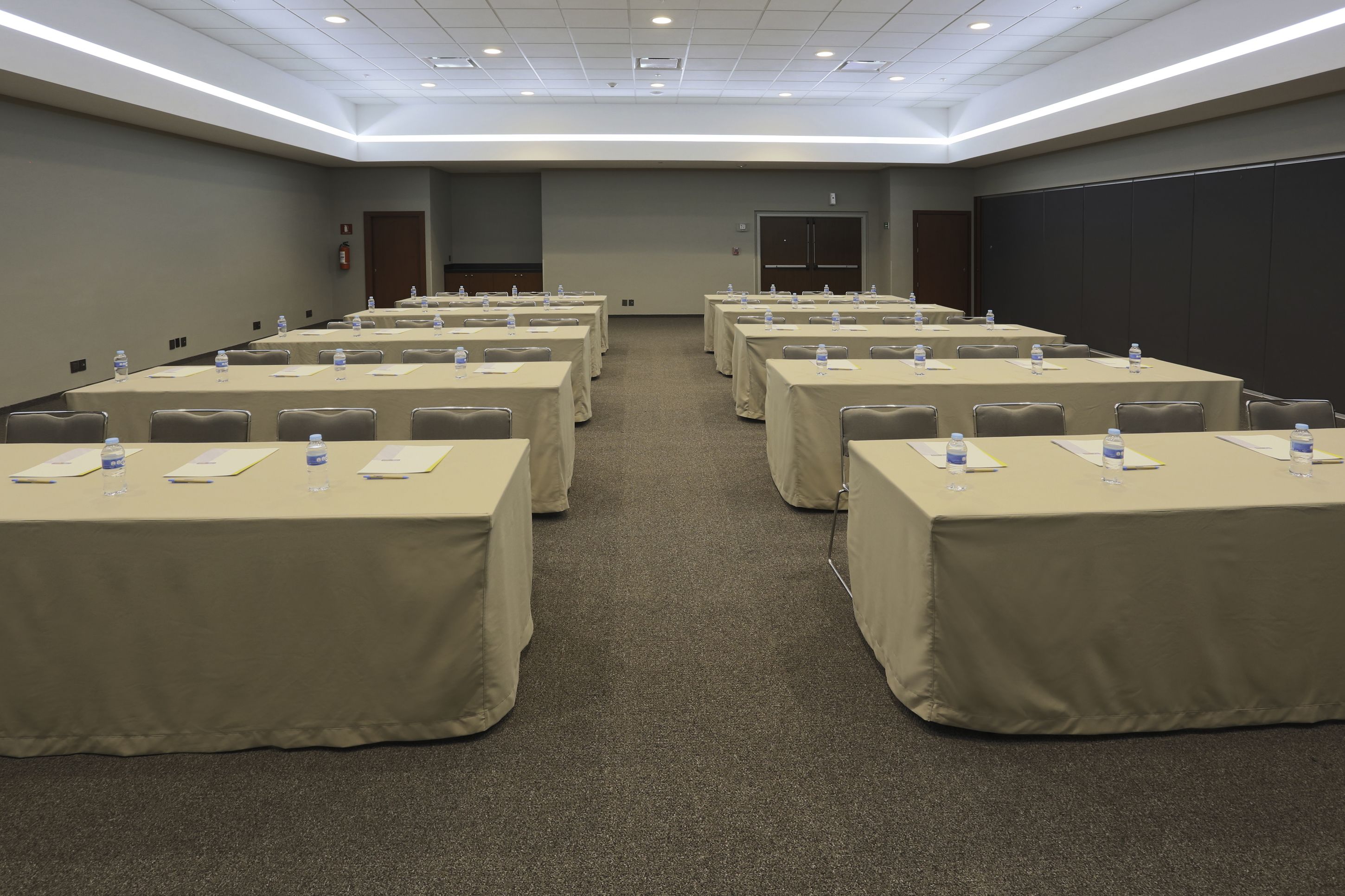 A conference room with multiple tables, each covered with a beige tablecloth, equipped with water bottles and nameplates.