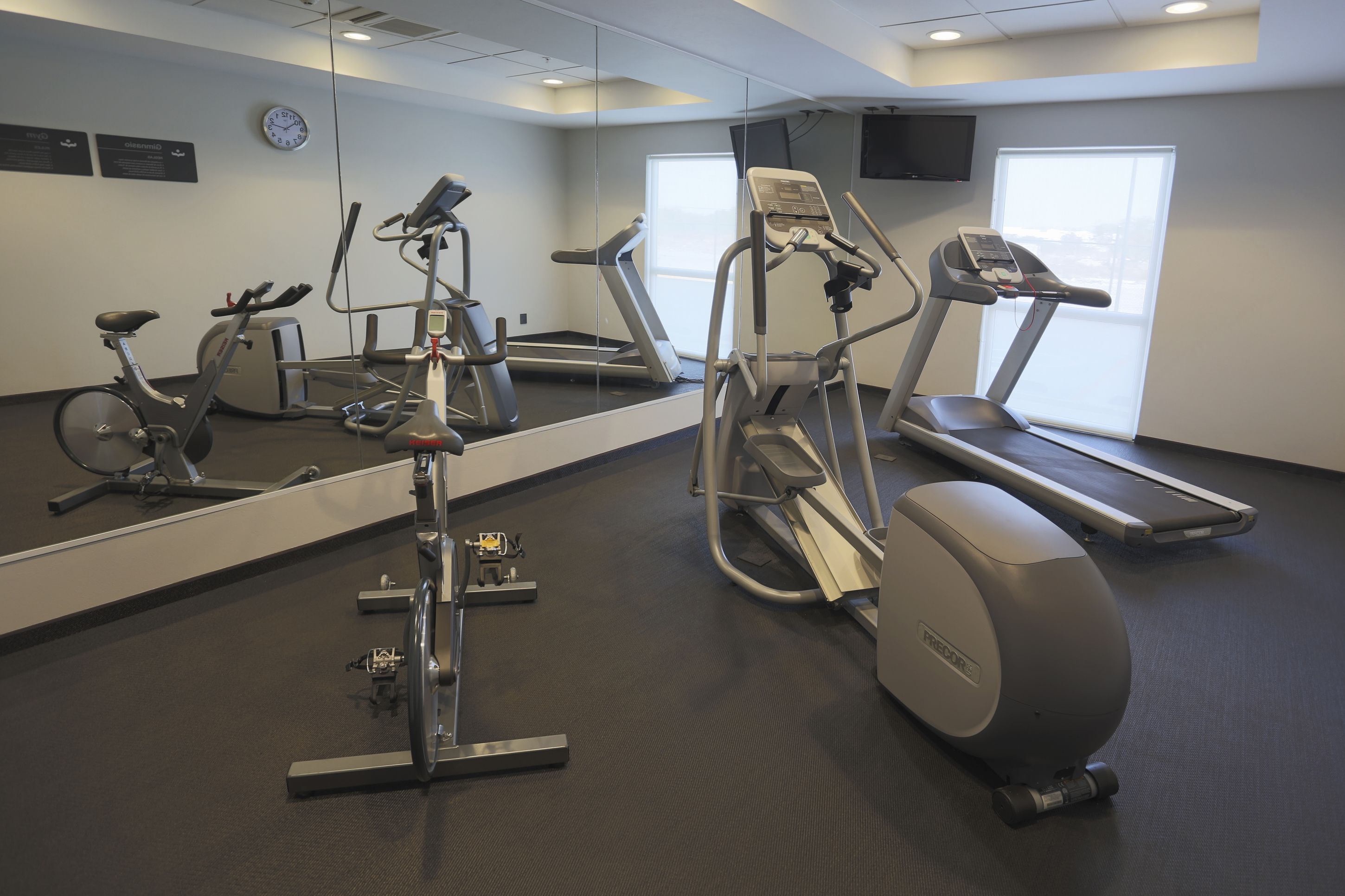 Un gimnasio con máquinas de cardio, una cinta de correr y un espejo grande.