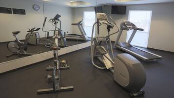 Un gimnasio con máquinas de cardio, una cinta de correr y un espejo grande.