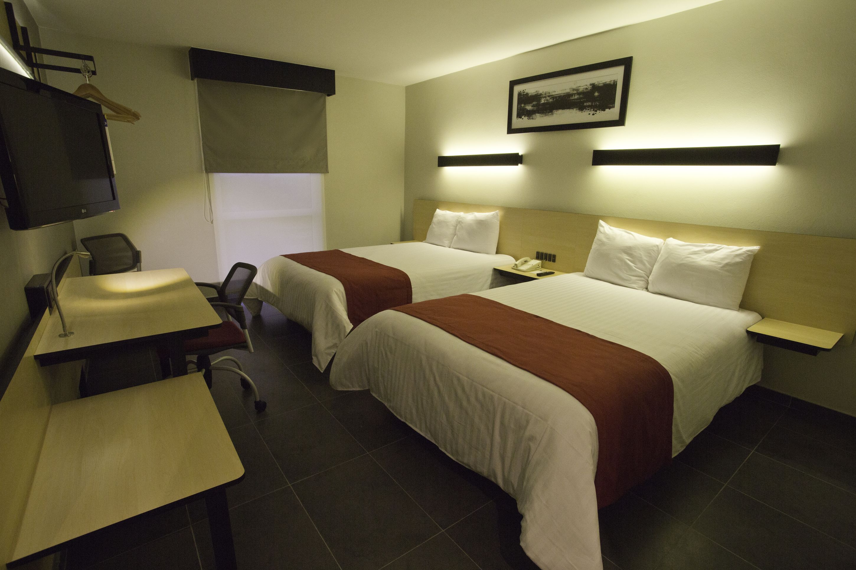 Ein Hotelzimmer mit zwei Betten, einem Schreibtisch, einem Sessel, einem Fernseher und einem Nachttisch.