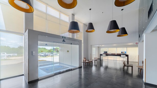 Een ruime lobby met een receptiebalie, een zithoek en een glazen lift.