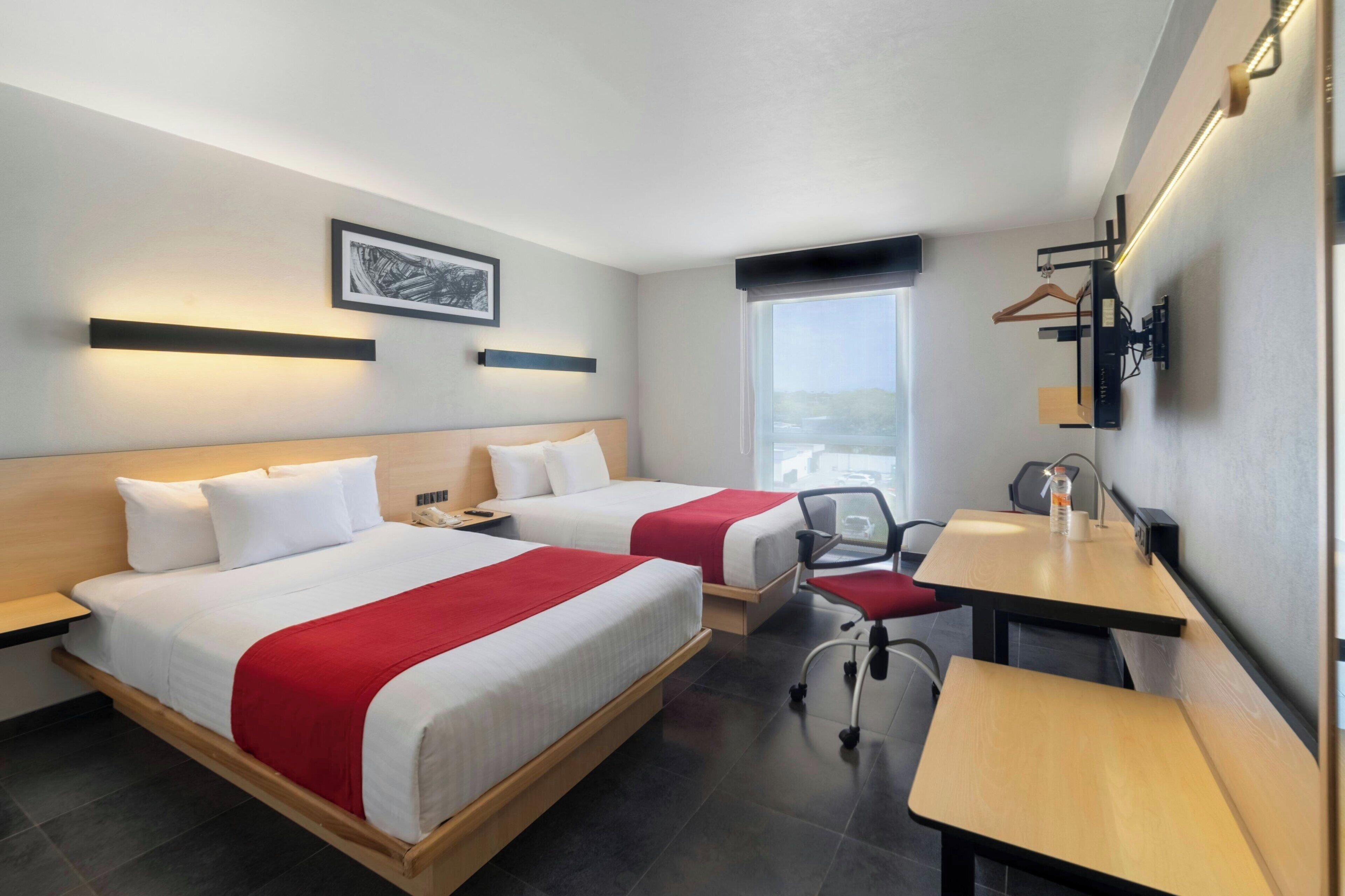 Habitación de hotel con dos camas, un escritorio, una silla y ventana con vistas.