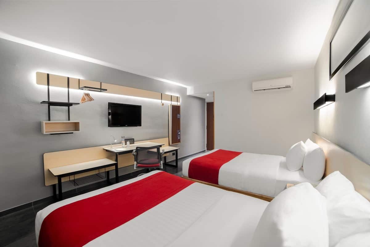Een hotelkamer met twee bedden, een bureau, een stoel, een televisie en een wandairconditioner.