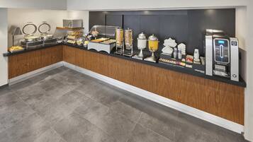 A buffet setup with various food stations, including a coffee machine and a juice dispenser.