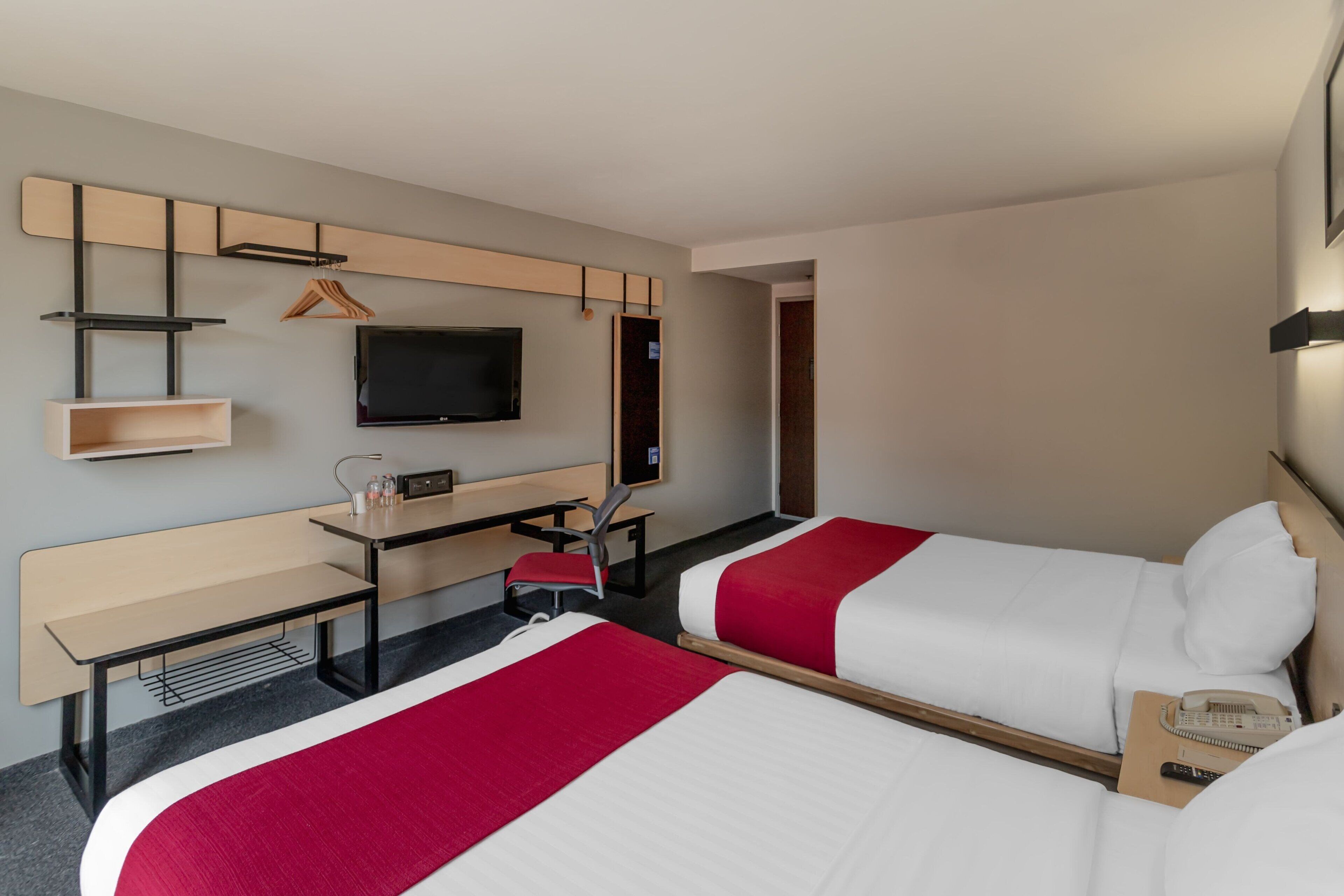 A hotel room with two beds, a desk, a chair, a TV, and a wardrobe.