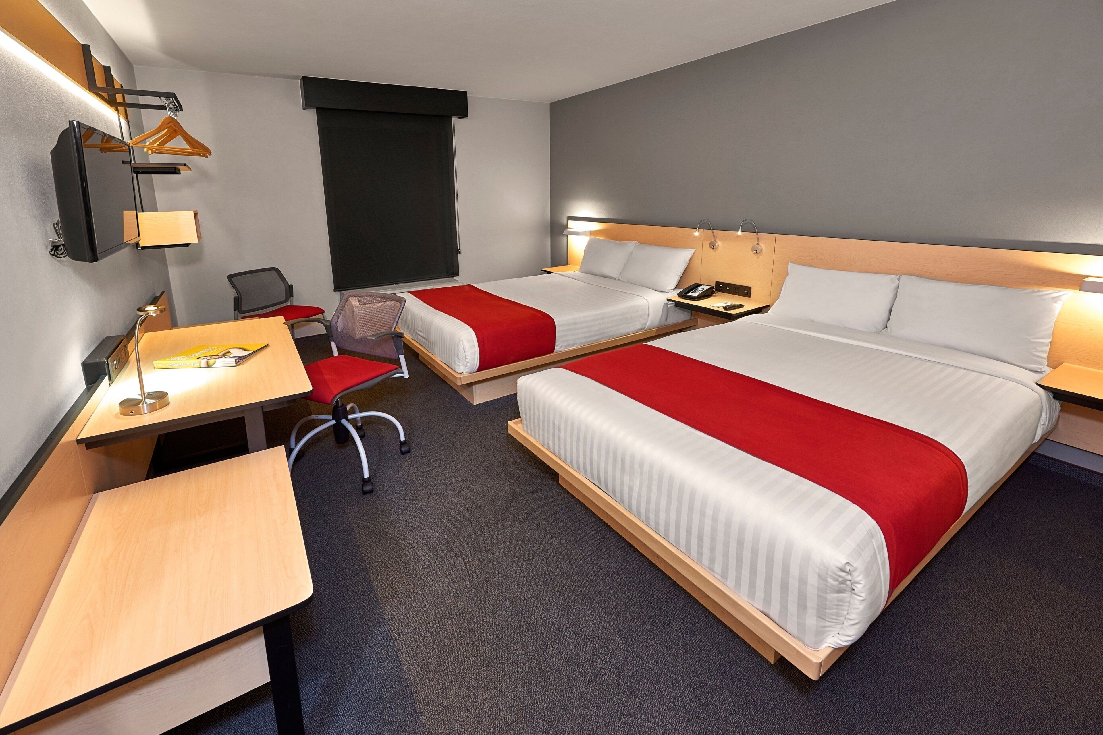 A hotel room with two beds, a desk, a chair, and a small table.