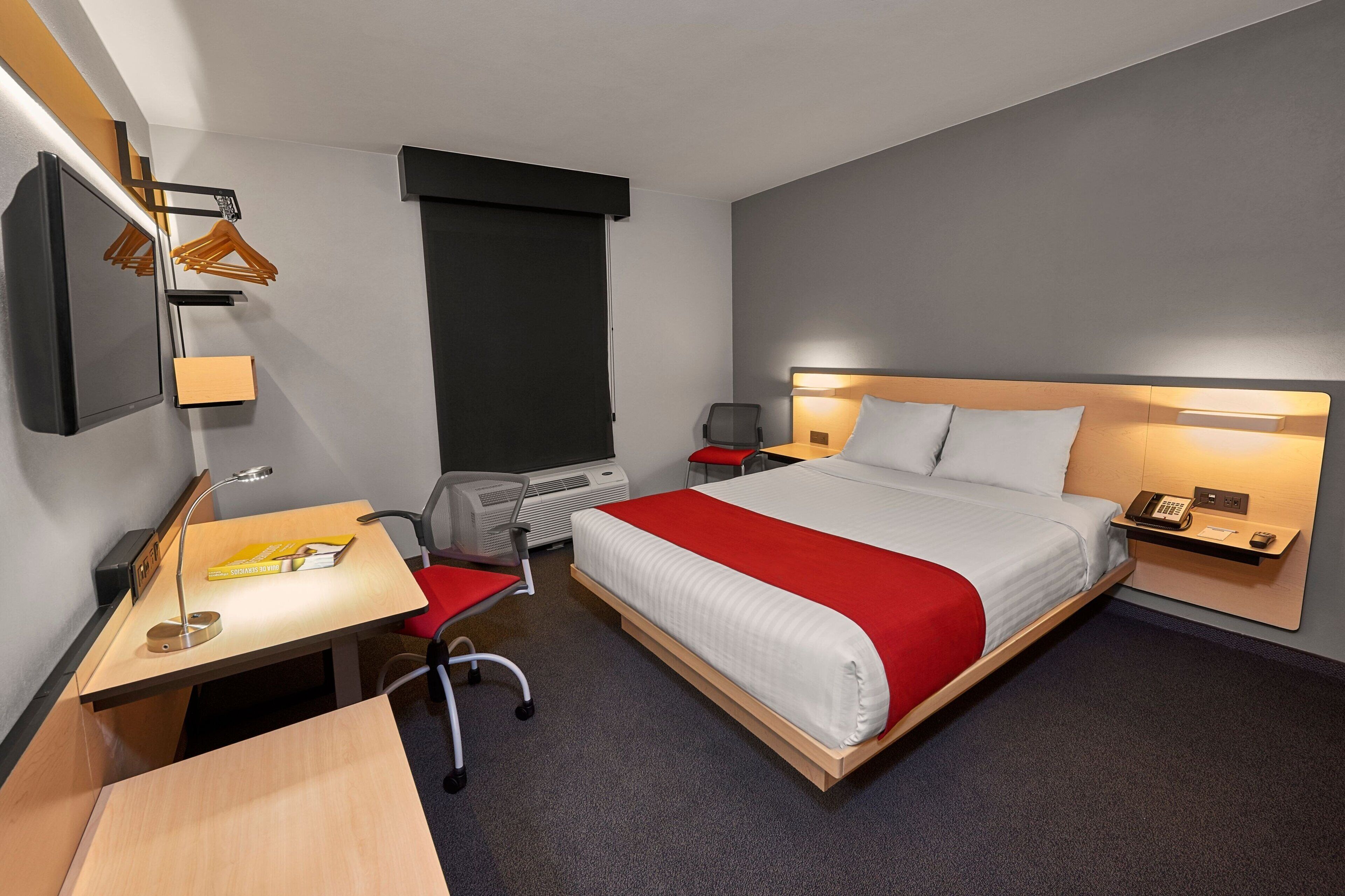 A hotel room with a bed, desk, chair, and a TV mounted on the wall.