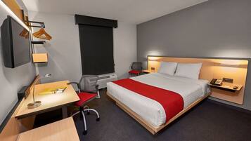 A hotel room with a bed, desk, chair, and a TV mounted on the wall.