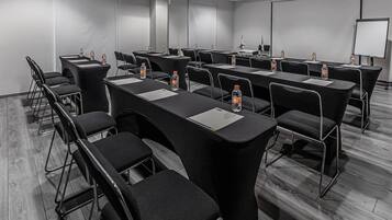 Un salón de conferencias con filas de sillas negras y mesas, cada una con una botella de agua y un bloc de notas.