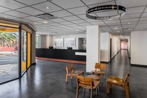 A modern hotel lobby with a reception desk, wooden chairs, and a large glass door leading outside. - City Express by Marriott Oaxaca (Oaxaca)