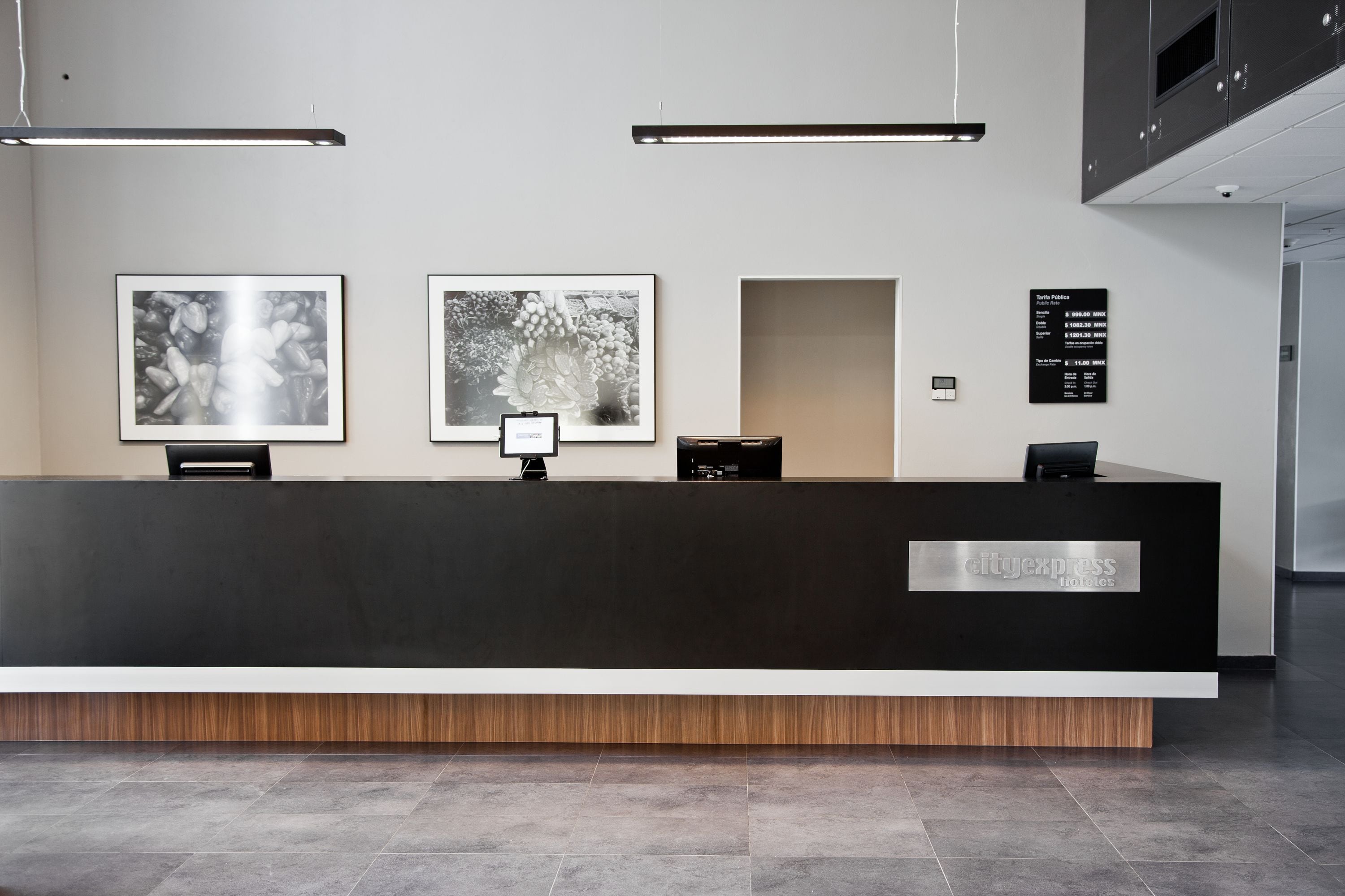 A modern hotel reception desk with framed artwork on the wall, a digital display, and a sign listing room rates.