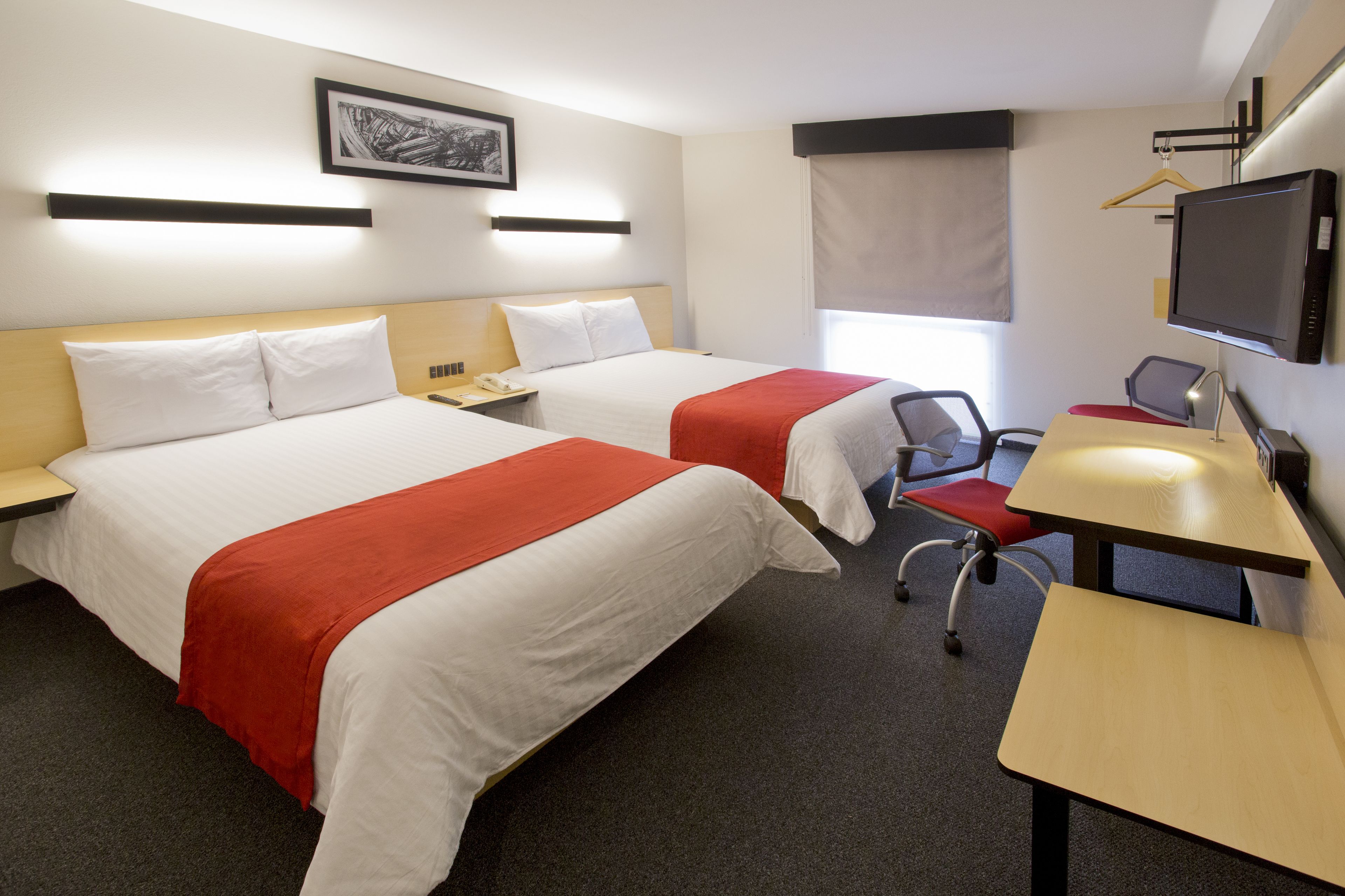 A hotel room with two beds, a desk, a chair, a TV, and a window with a curtain.