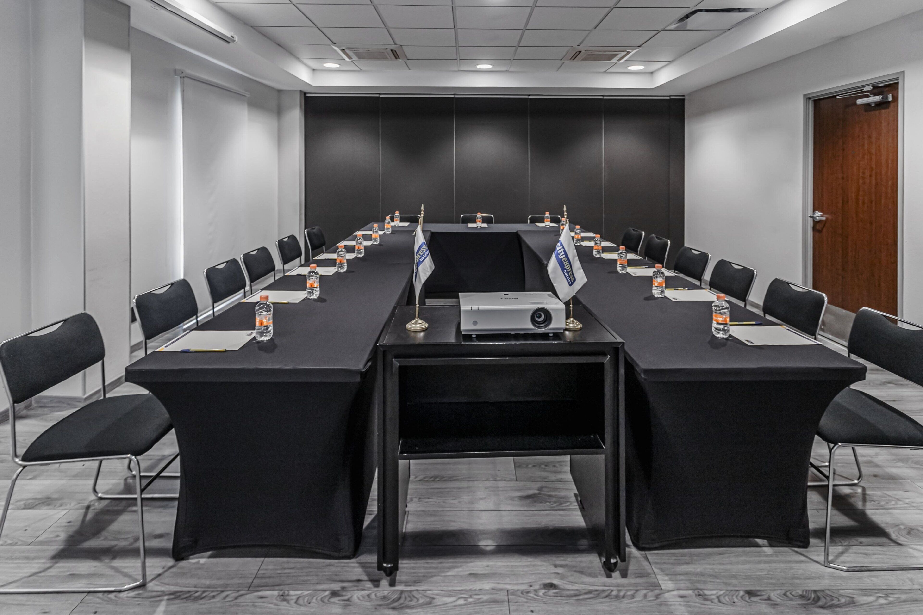 Un salón de conferencias con una larga mesa, sillas negras y un proyector.