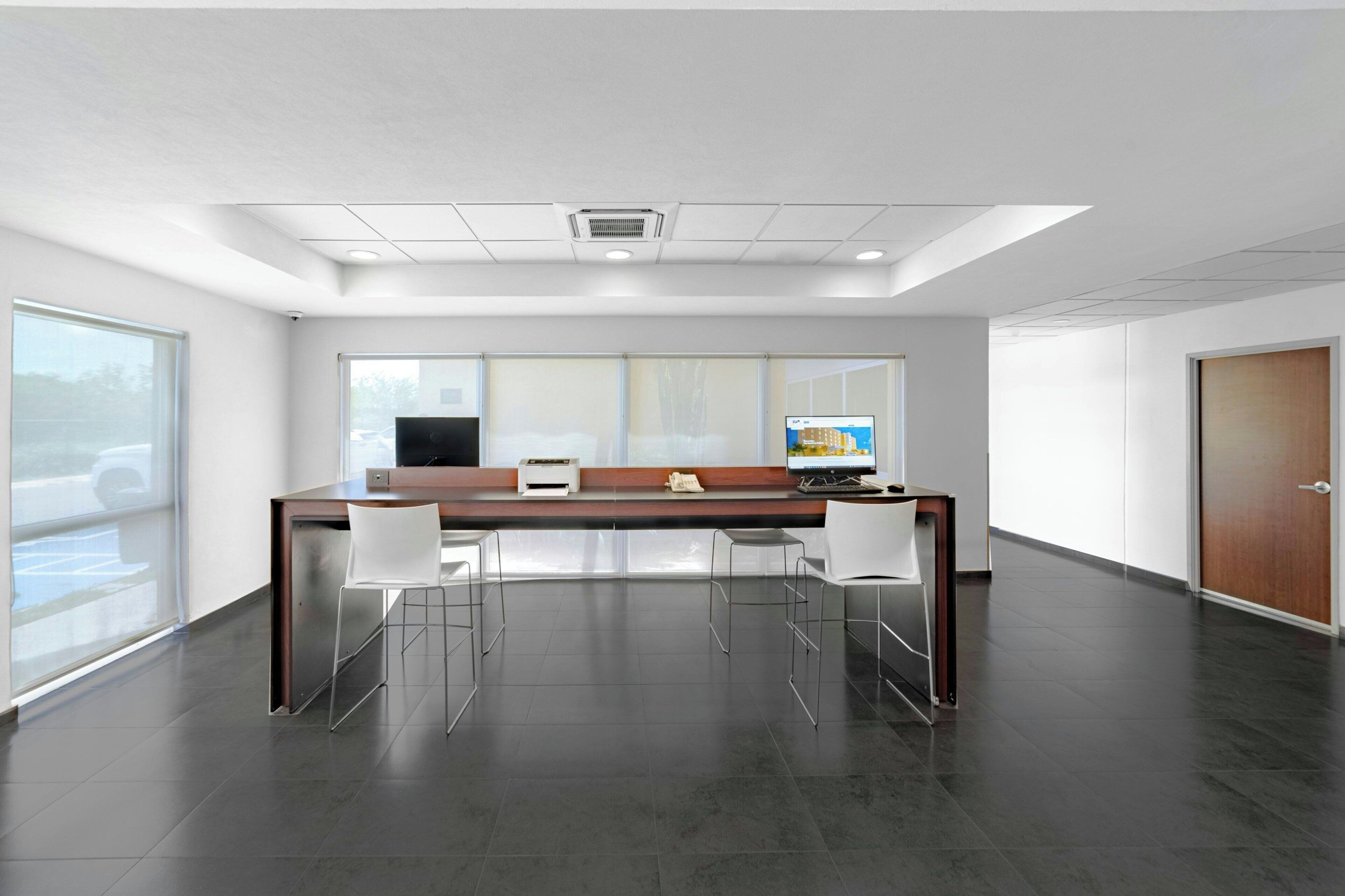 A modern office with a long table, white chairs, and a computer.