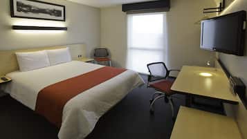 A hotel room with a bed, a desk, a chair, a television, and a window.