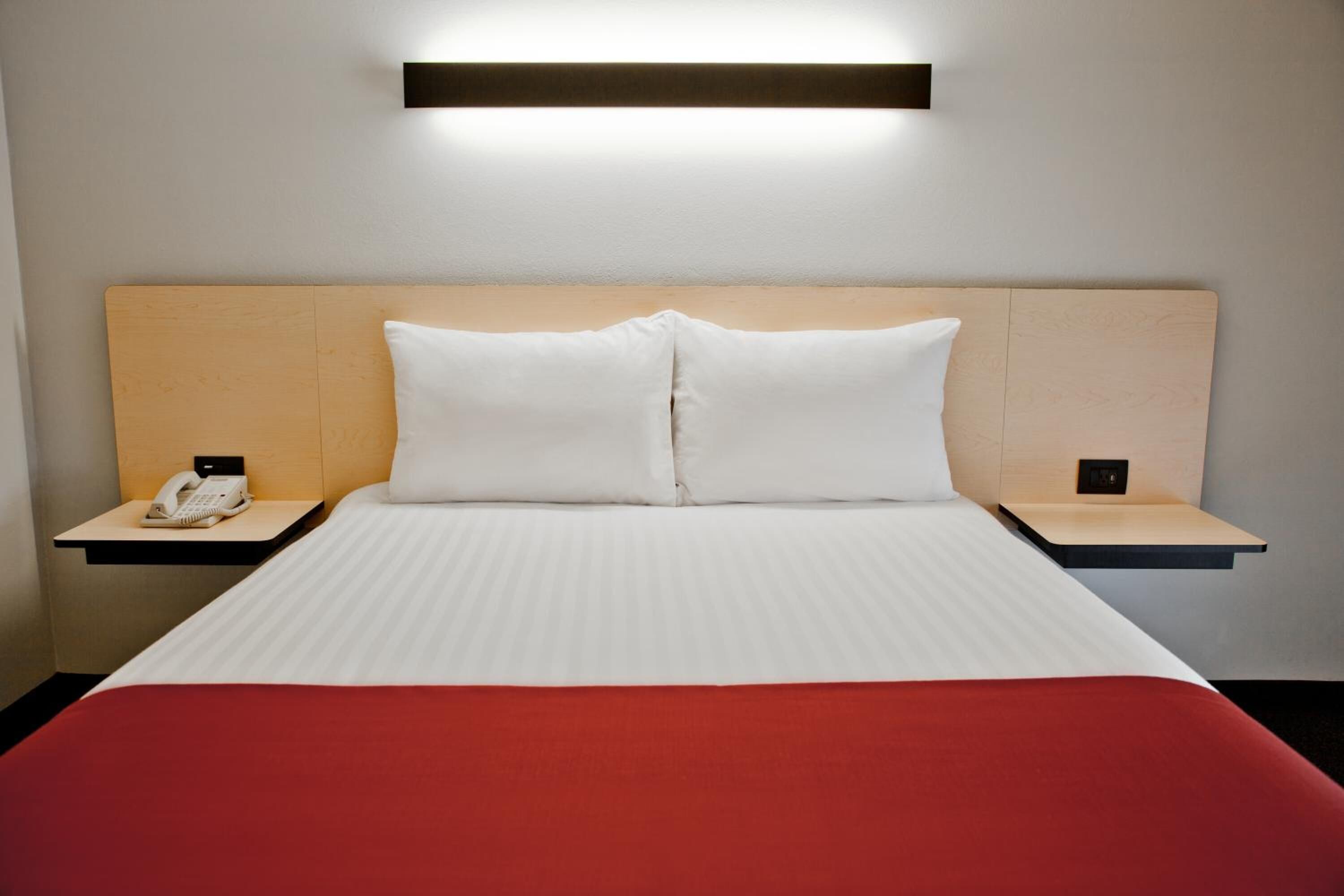 Habitación de hotel con una cama, dos mesitas de noche, un teléfono y una lámpara fijada a la pared.