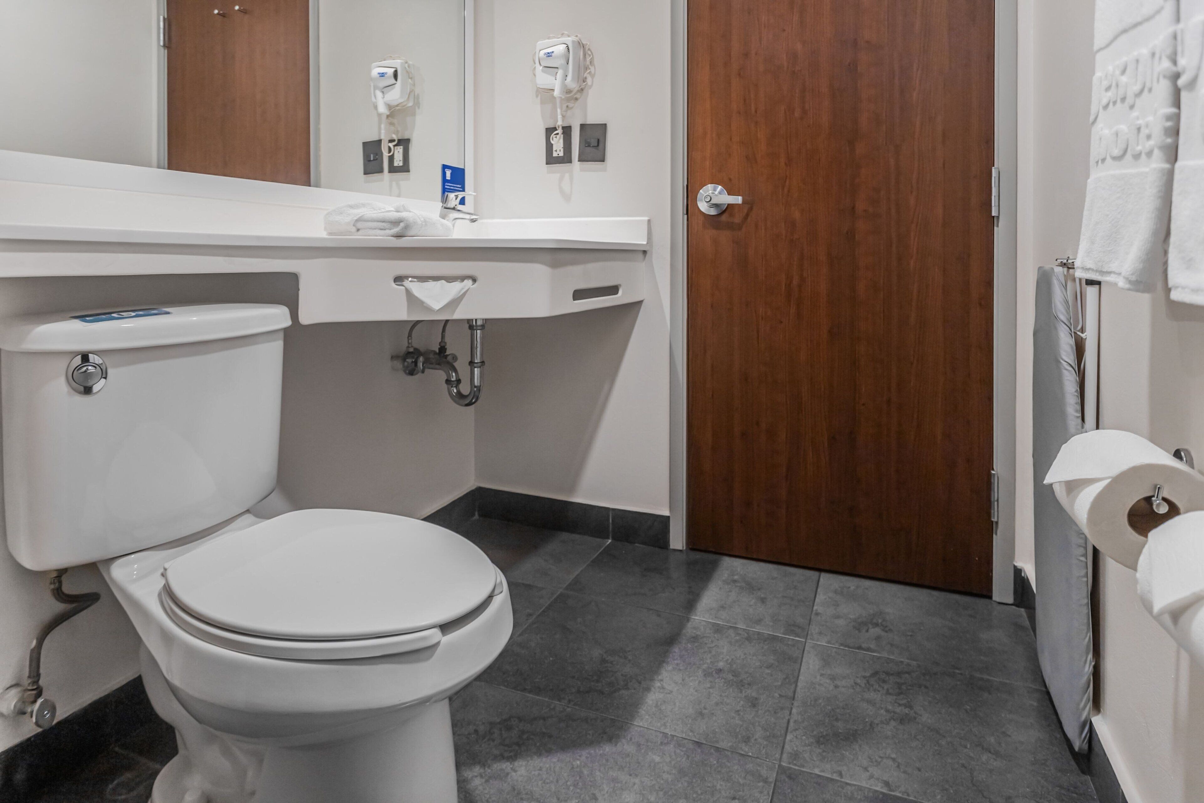 A modern bathroom with a white toilet, a sink with a towel dispenser, and a shower area.