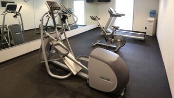 Un gimnasio con máquinas de cardio, un dispensador de agua y un reloj en la pared.