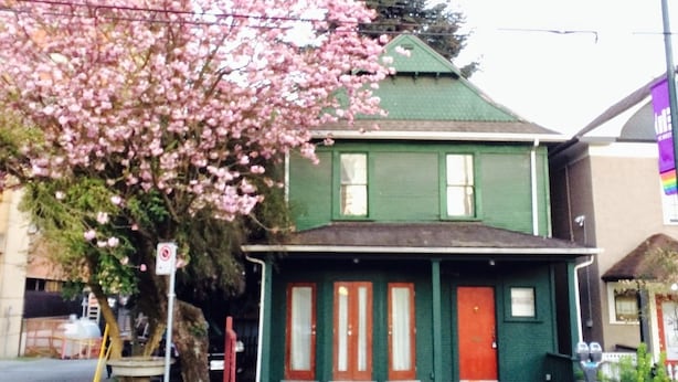 Een groen huis met een rode deur, een boom met roze bloemen en een voetpad.