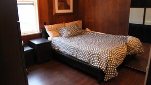 Een slaapkamer met een bed, houten vloer, een nachtkastje, een raam en een lijst met een afbeelding aan de muur.