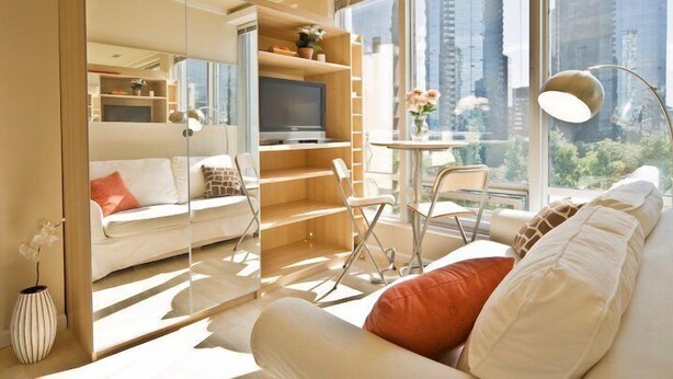 A modern living room with a sofa, TV, and a dining area with chairs and a table. - MondeLiving City Condo (Vancouver)