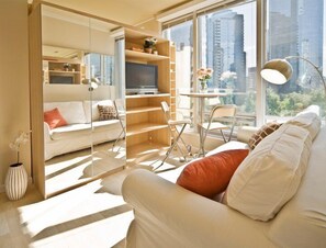 A modern living room with a sofa, TV, and a dining area with chairs and a table. - MondeLiving City Condo (Vancouver)