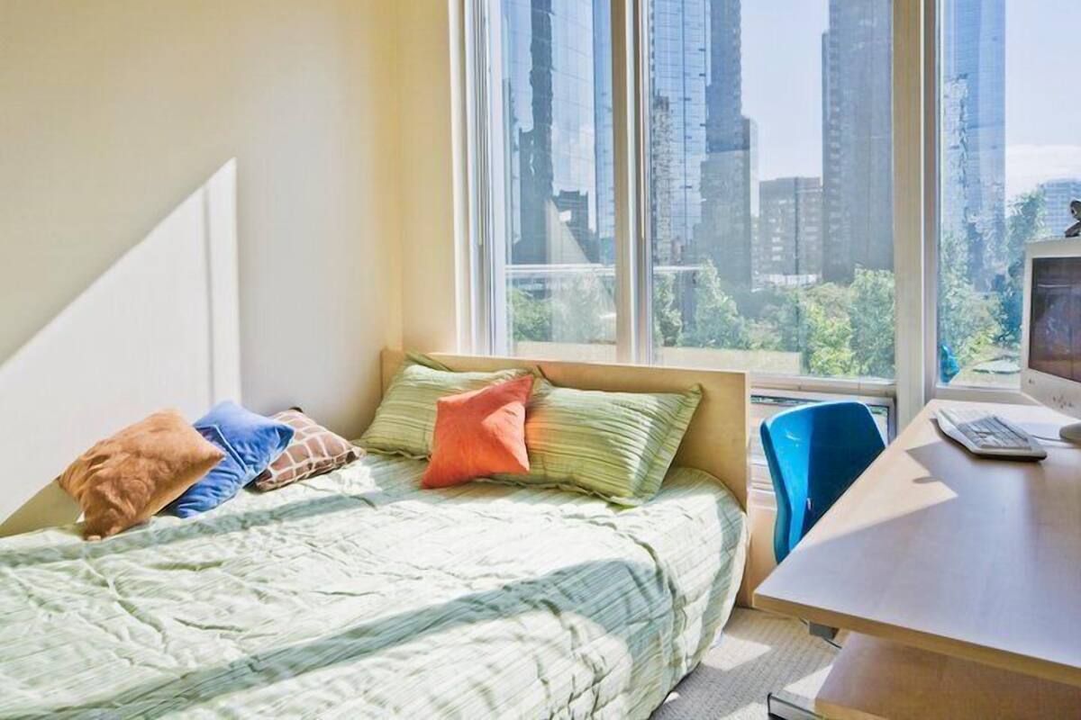 A bedroom with a bed, pillows, a desk, and a computer.