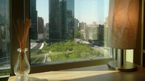 A view from a window with a lamp on a table, a vase with reeds, and a cityscape with tall buildings and greenery. - MondeLiving City Condo (Vancouver)