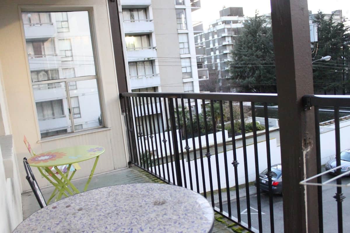 A balcony with a small table and chair, a view of a street with cars, and a building in the background.