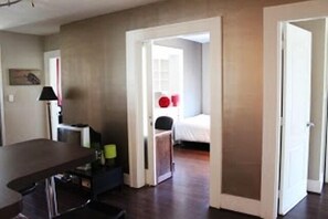 A room with a desk, chair, and a bed. There is a door leading to another room. - MondeLiving Robson Living (Vancouver)