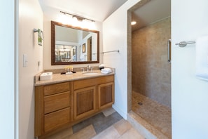 Un baño con tocador de madera, un espejo grande y zona de ducha.