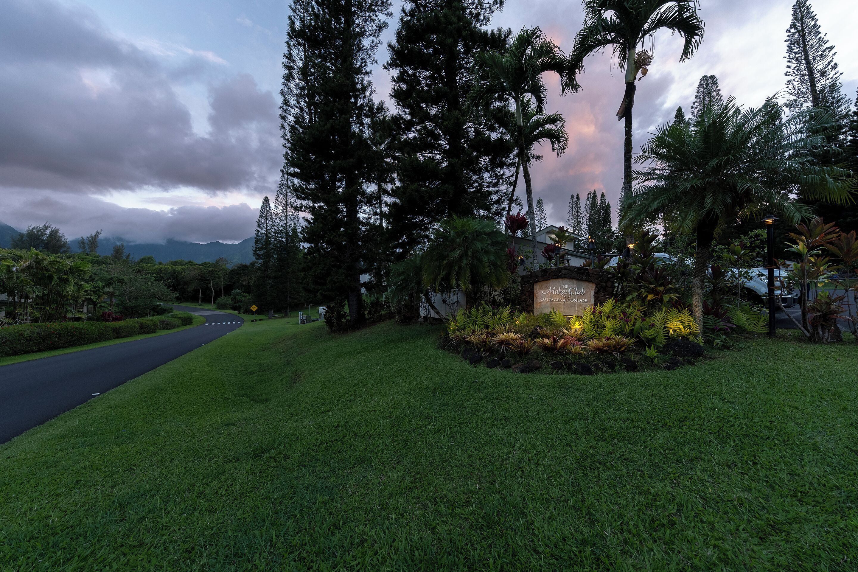 A well-maintained grassy area with a sign for 'Makai Club Cottages & Condos' and a curved road in the background.