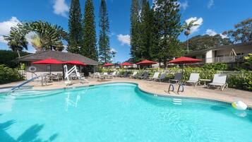 Relax by the serene pool surrounded by lush greenery and tall pine trees, with lounge chairs and umbrellas providing shade.