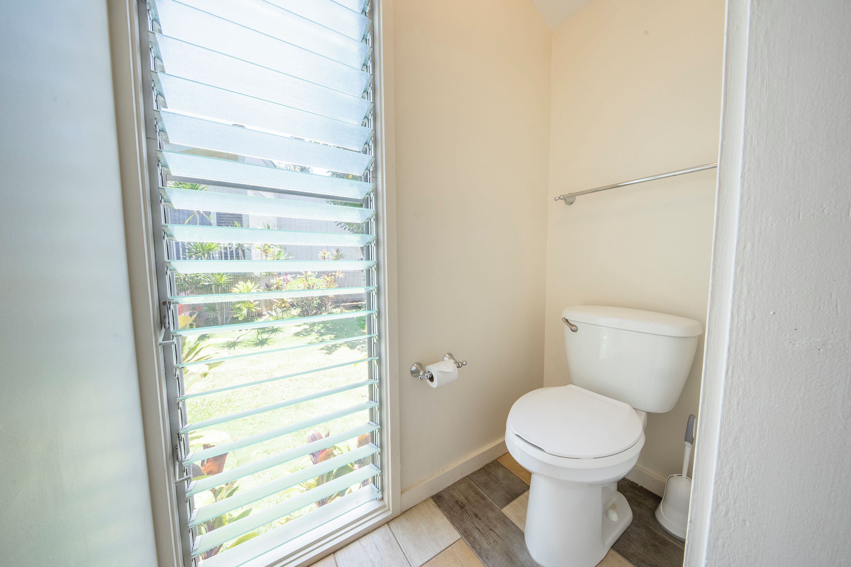 A bathroom with a toilet, a roll of toilet paper, and a window with blinds.