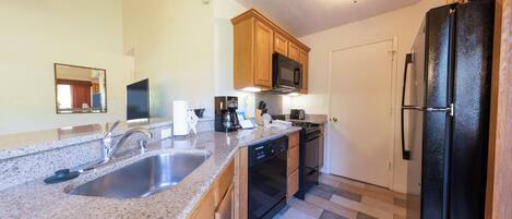 A kitchen with granite countertops, wooden cabinets, a stainless steel sink, a black refrigerator, and a built-in microwave.
