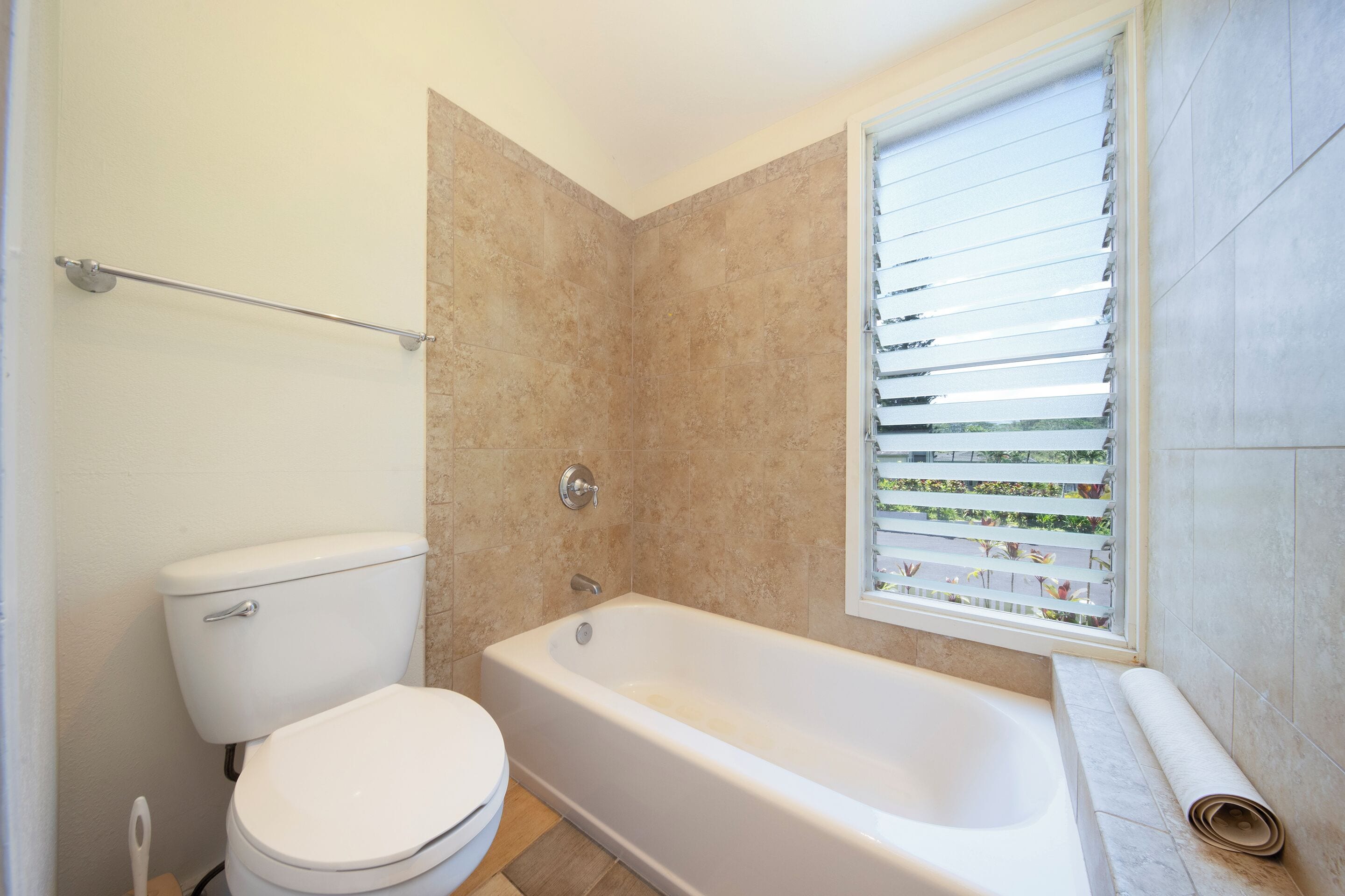 Un baño con inodoro, bañera y ventana con persianas.